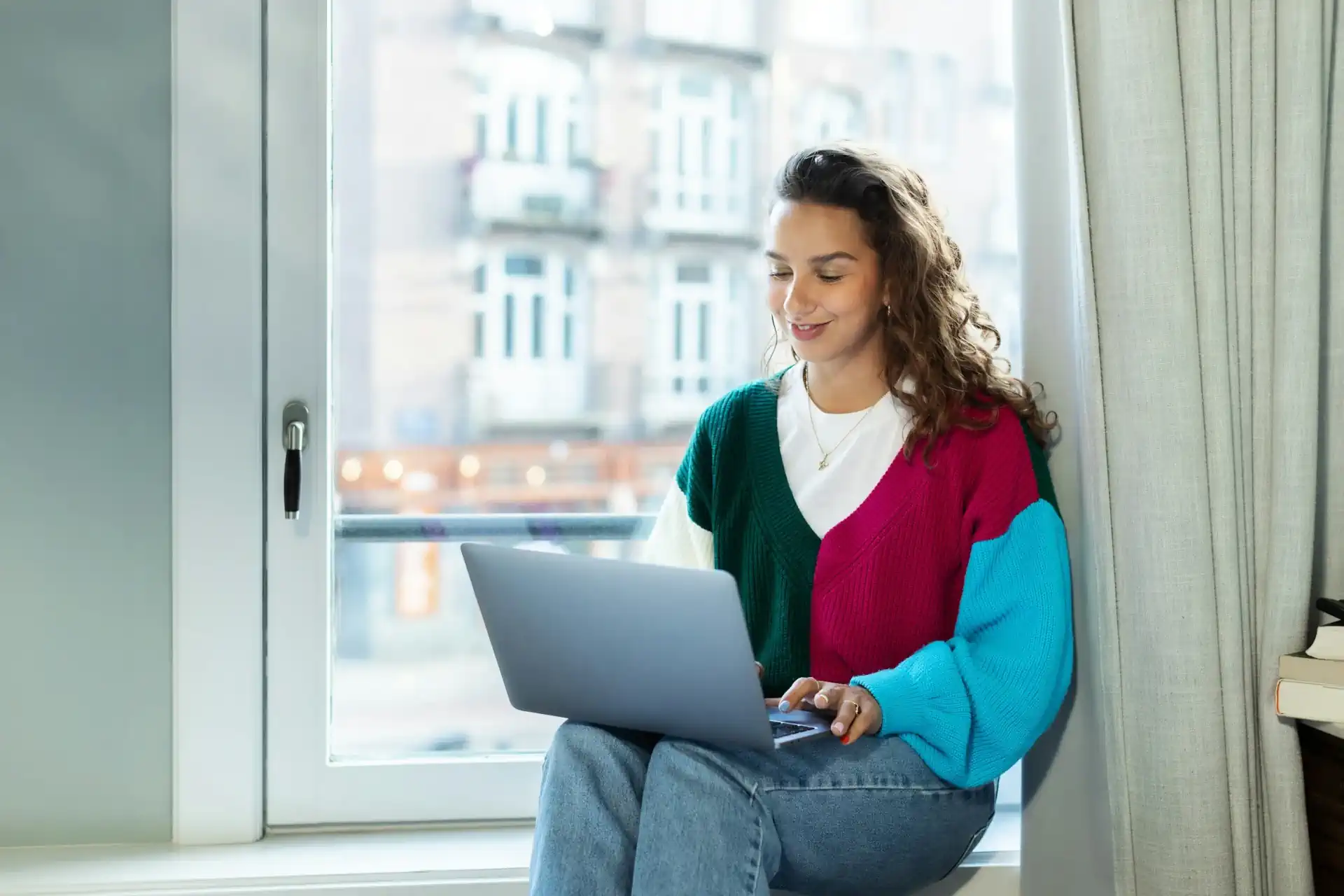 Een vrouw zit in de vensterbank van een kantoor en heeft een laptop op schoot